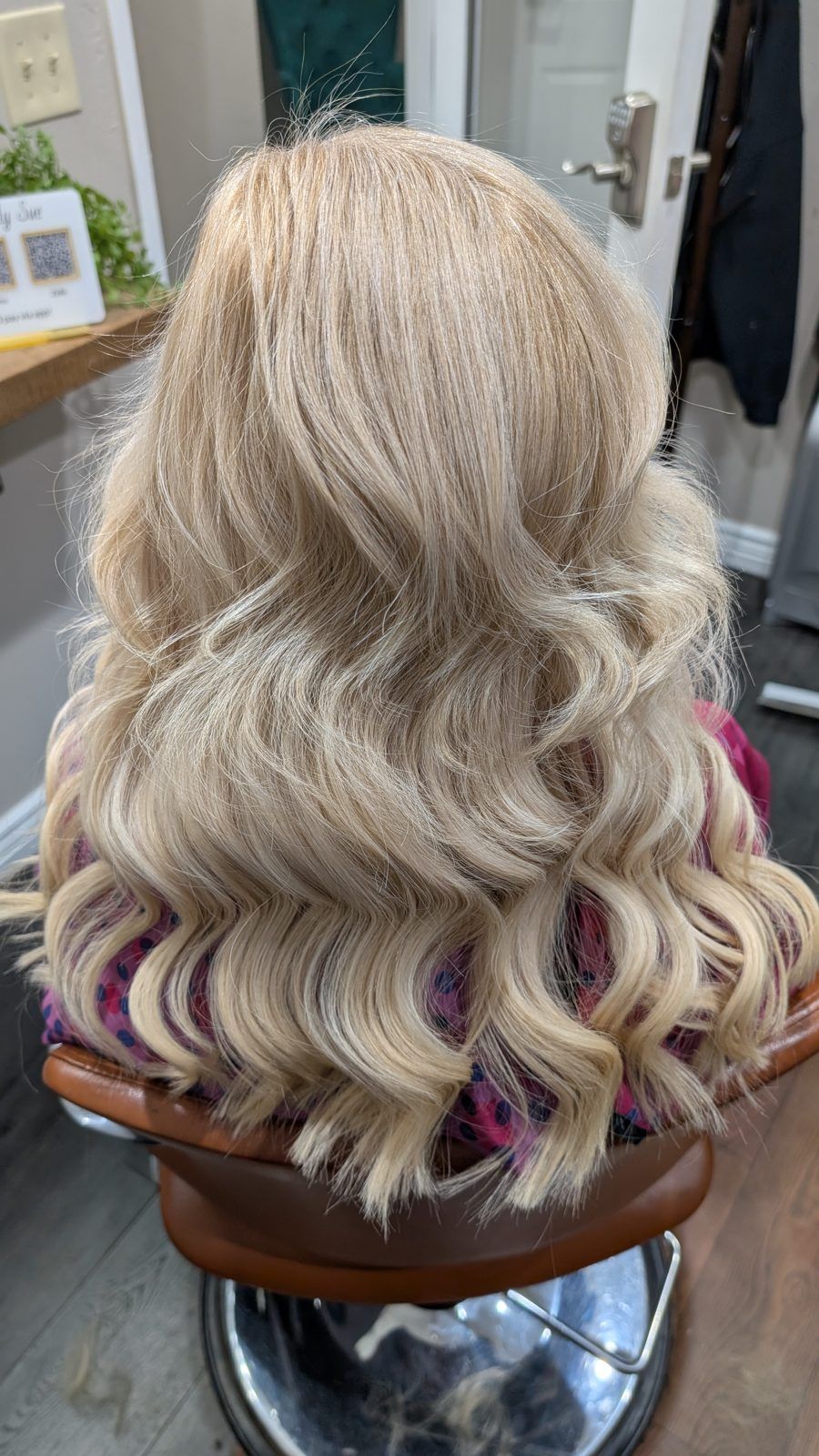 Voluminous soft blonde curls with subtle dimension, shown from behind in the salon.