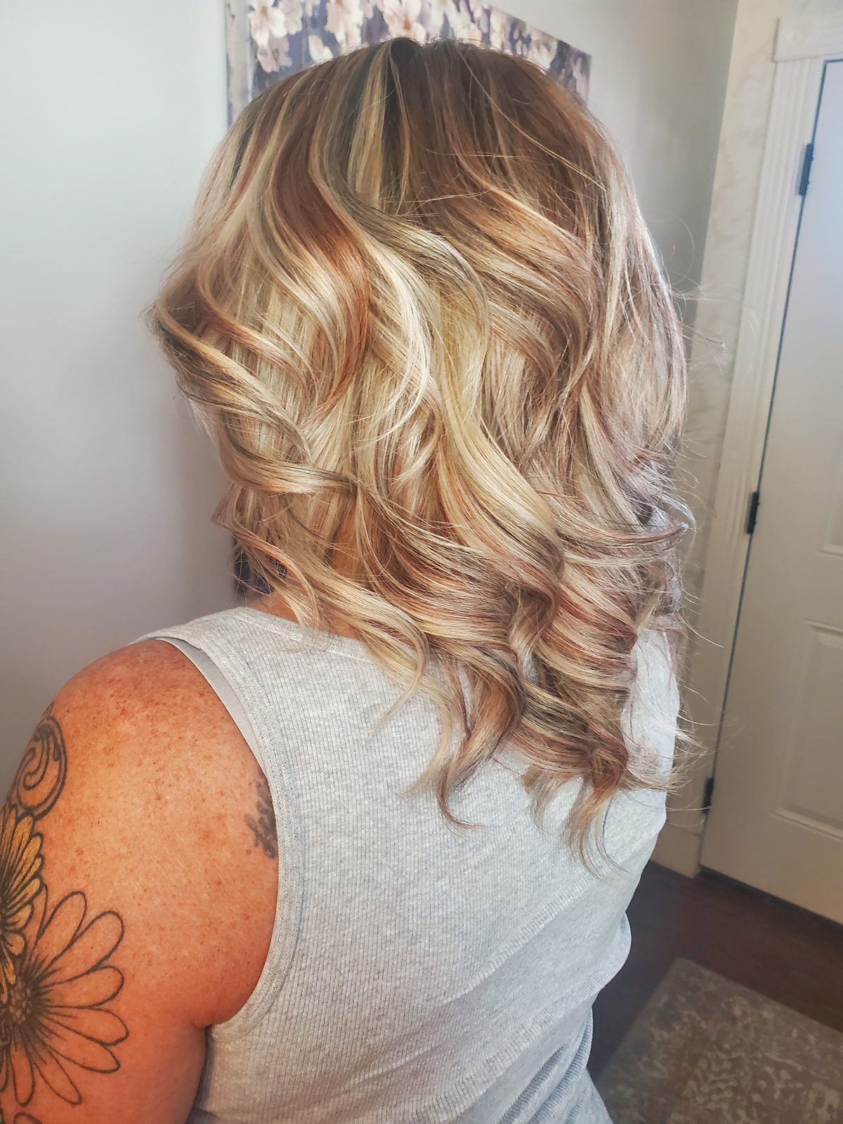 Shoulder-length blonde waves with warm copper and ash-brown dimensional lowlights, shown from the side.