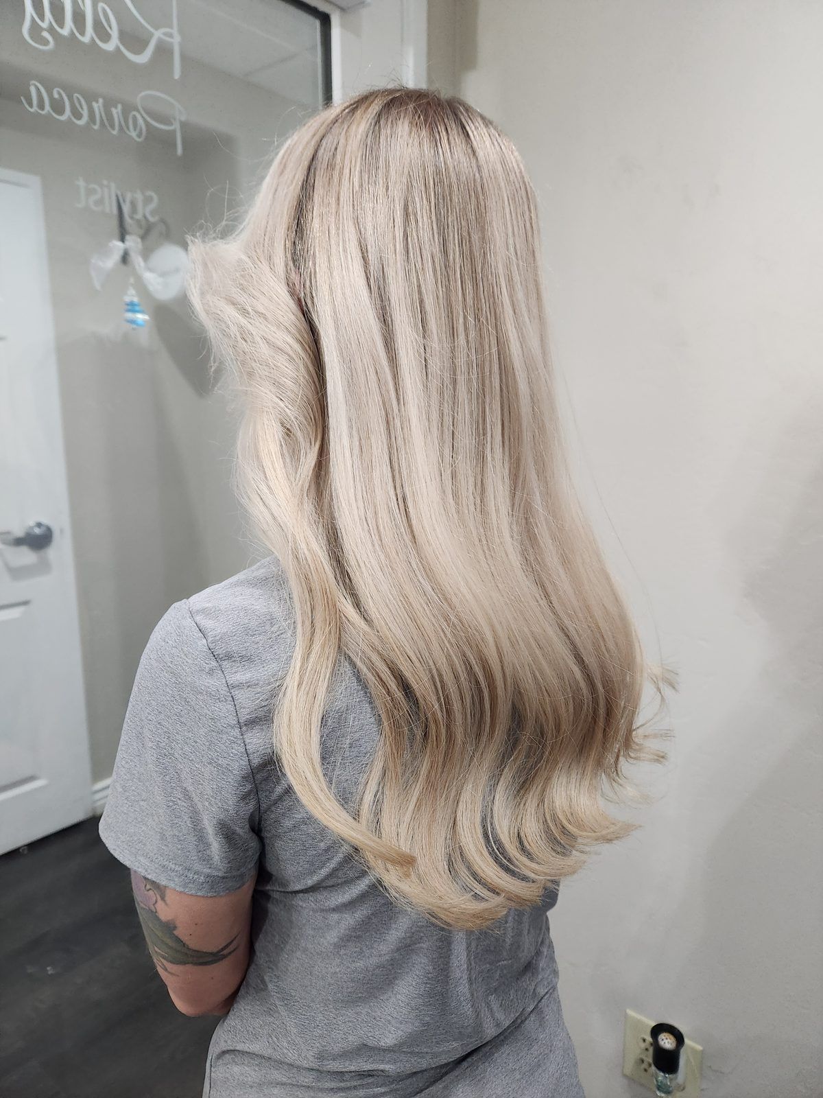 Long creamy blonde with a soft shadow root and curled ends, shown from the side.