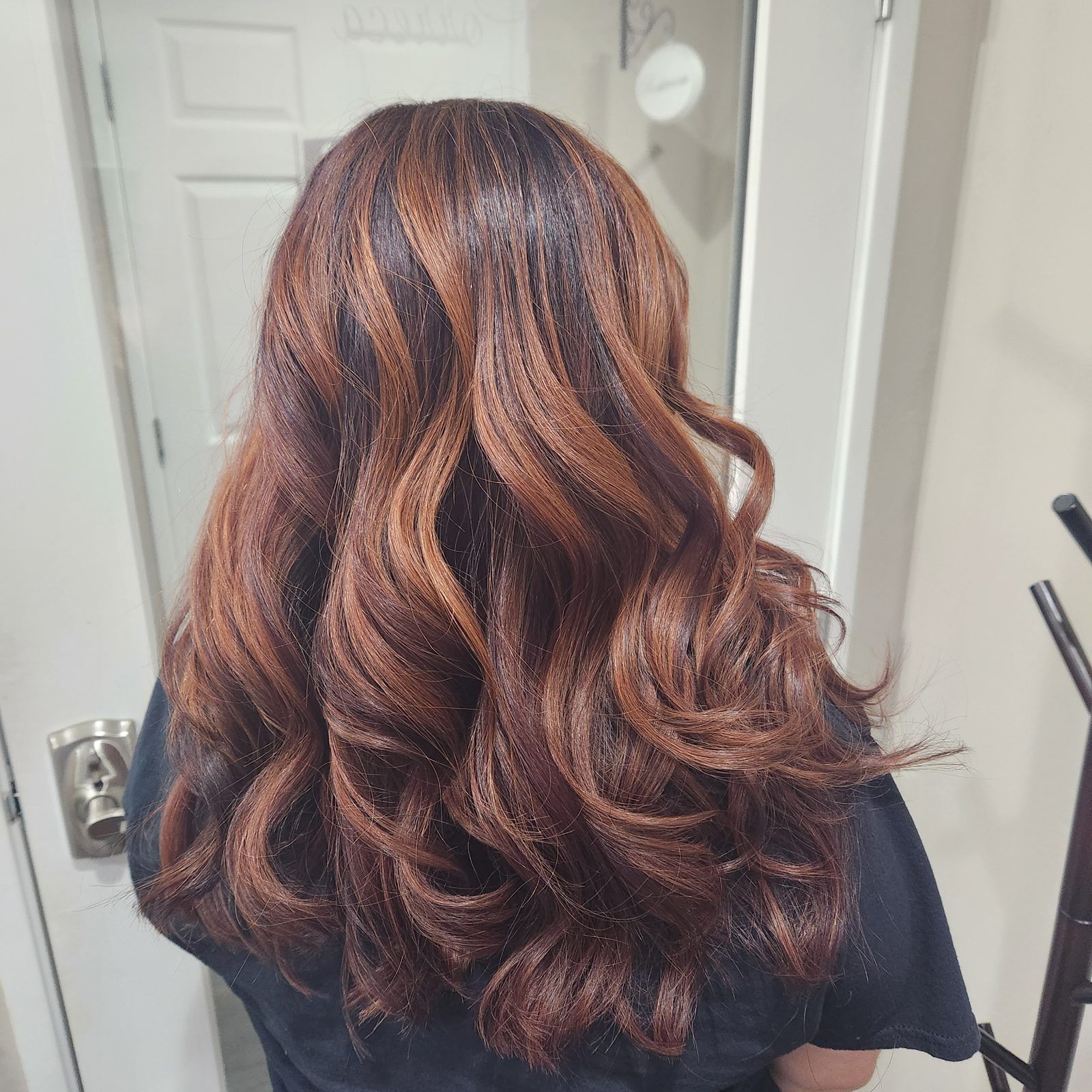 Dark espresso hair with copper and caramel balayage in glossy waves, shown from behind.